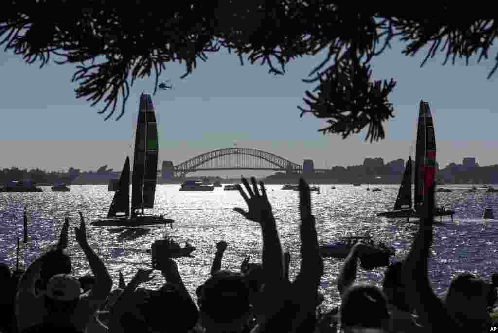 People cheer as Australia SailGP Team and ROCKWOOL Denmark SailGP Team sail past Genesis Island with Sydney Harbour Bridge in the distance on Race Day 2 of the KPMG Australia Sail Grand Prix in Sydney.
