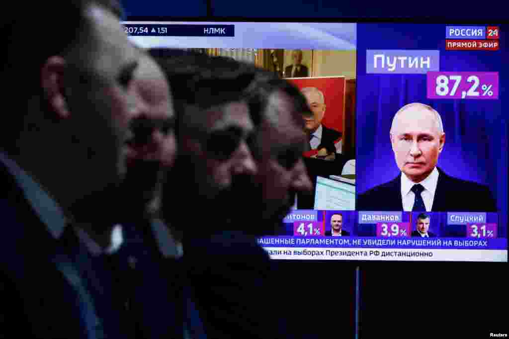 Men sit near a TV broadcasting news on the results of Russian presidential candidate and incumbent President Vladimir Putin, on the final day of the presidential election in Moscow, March 17, 2024.