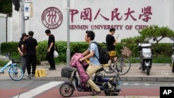 北京街頭人們經過中國人民大學校園外牆的標誌。 （2024年7月22日）