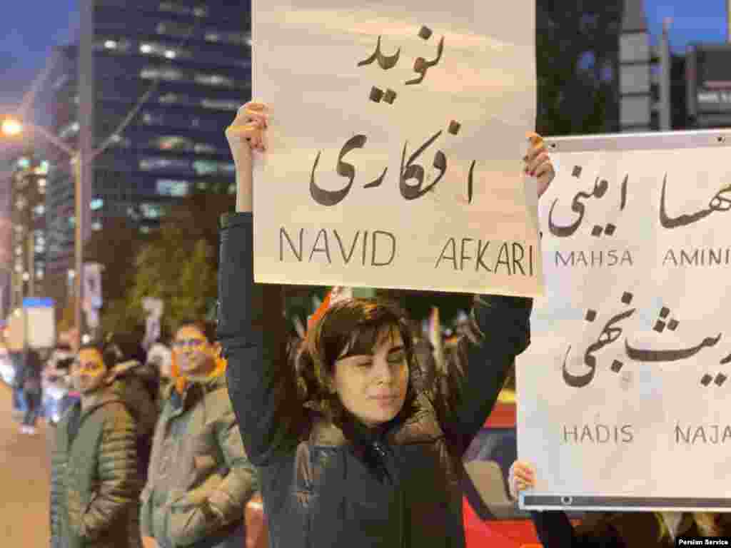 یک زن شرکت کننده پلاکاردی با نام نوید افکاری را حمل می‌کند تا نام او را یادآور شود.