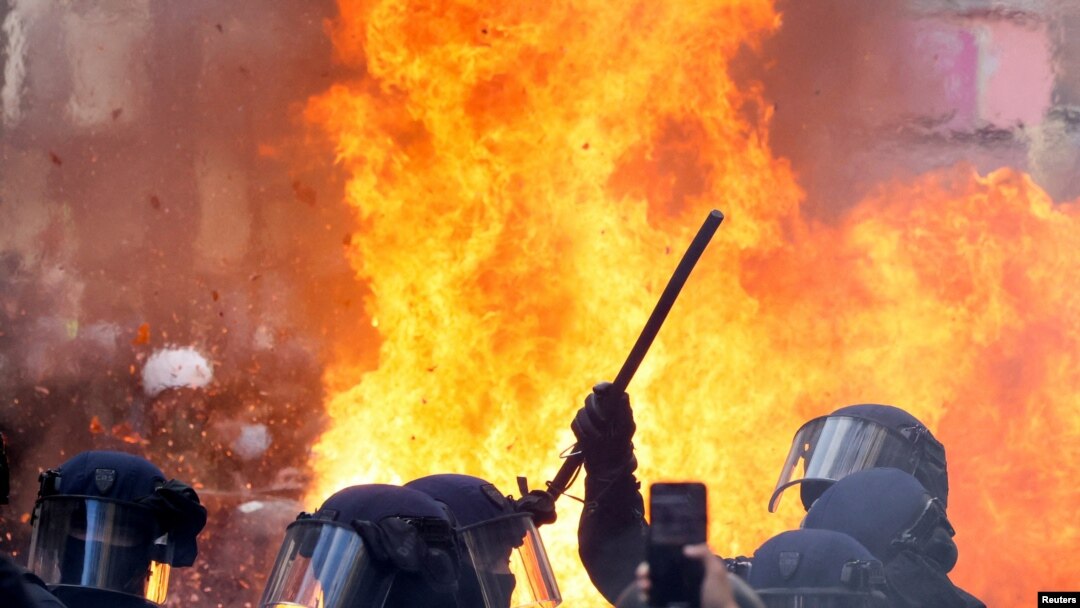 Flames from a fire rise behind law enforcement officers during a demonstration against the French government's pension reform plan as part of the fourth day of national protests, in Paris, France, Feb. 11, 2023.