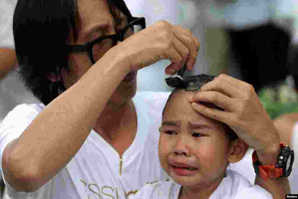 A devotee girl has her hair shaved by her father during a mass novice nun ordination ceremony to mark the first anniversary of late Thailand's King Bhumibol Adulyadej's death, at the Sathira-Dhammasathan Buddhist meditation center in Bangkok.