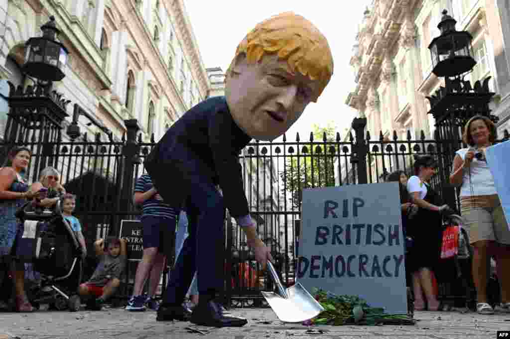 A demonstrator wearing a mask depicting Britain's Prime Minister Boris Johnson stands beside a mock gravestone inscribed with the words "RIP British Democracy" outside the gates to Downing Street in central London.