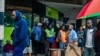 Residents walk in a street as others queue outside a bank in Harare, Nov. 15, 2017.