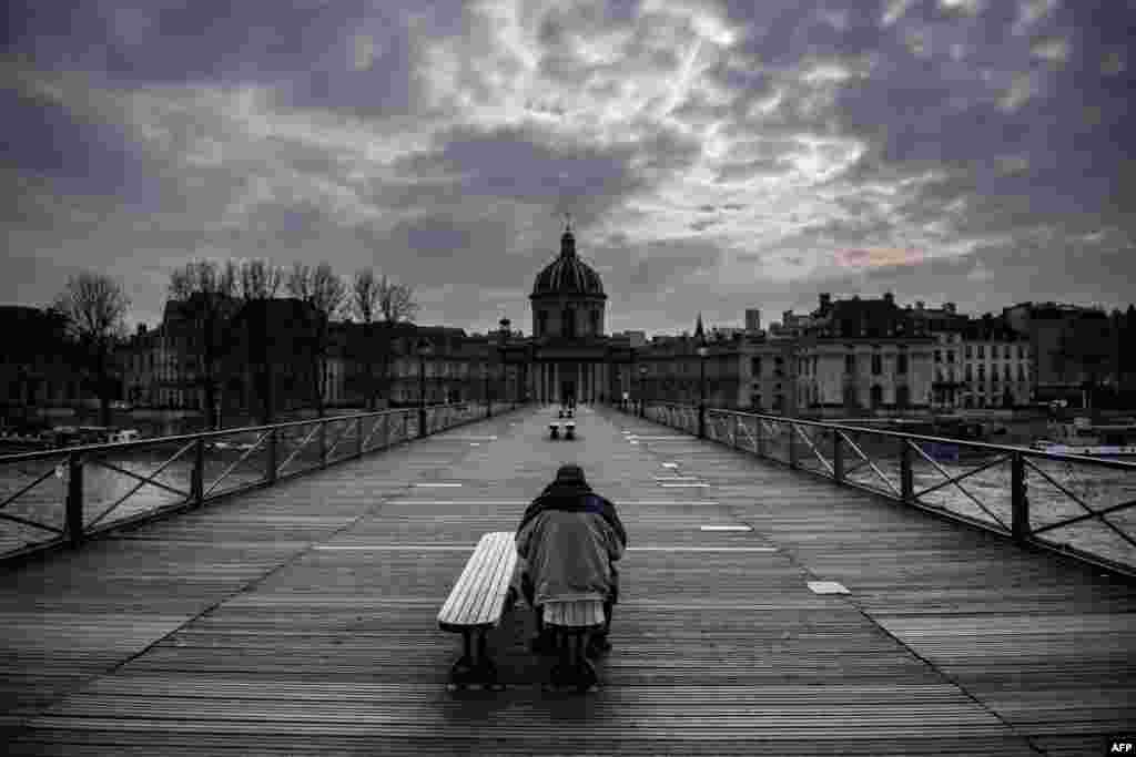 A man sits on a bench of the Pont Des Arts in Paris as a strick lockdown comes into in effect to stop the spreading of the COVID-19 in France.