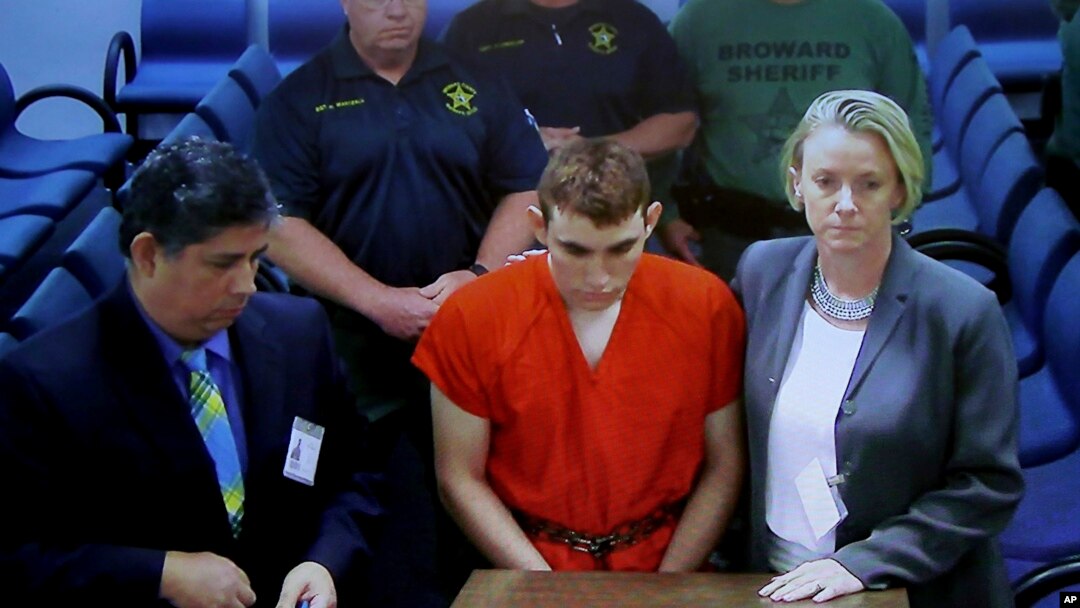 စွဲချက် ၁၇ ခုနဲ့ စွပ်စွဲခံထားရတဲ့ Nikolas Cruz ကို လက်တွေကို ခါးမှာသံကြိုးနဲ့ချည်ထားပြီး လိမ္မော်ရောင် ထောင်ဝတ်စုံနဲ့ ဖလော်ရီဒါပြည်နယ်က တရားရုံးတခုမှာ တွေ့ရစဉ်။