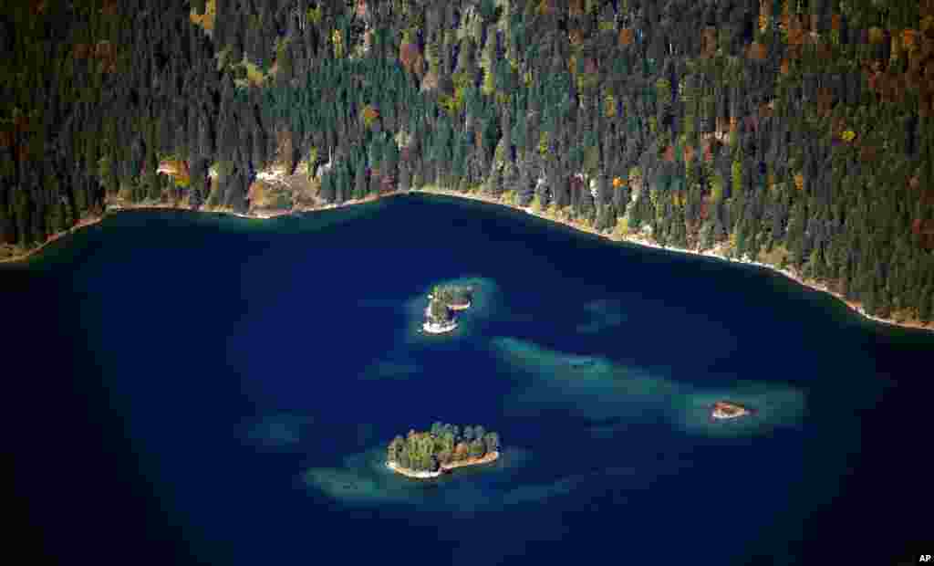 The sun shines over the deep blue lake Eibsee and the autumnally colored trees in the valley of Germany's highest mountain, the Zugspitze near Garmisch-Partenkirchen.