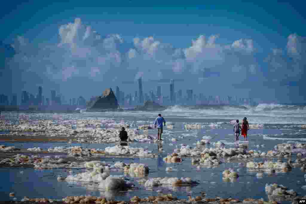 Tourists walk on the Currumbin Beach covered with foam in the wake of cyclonic conditions after wild weather lashed Australia's Northern New South Wales and South East Queensland with heavy rain, strong winds and king tides.