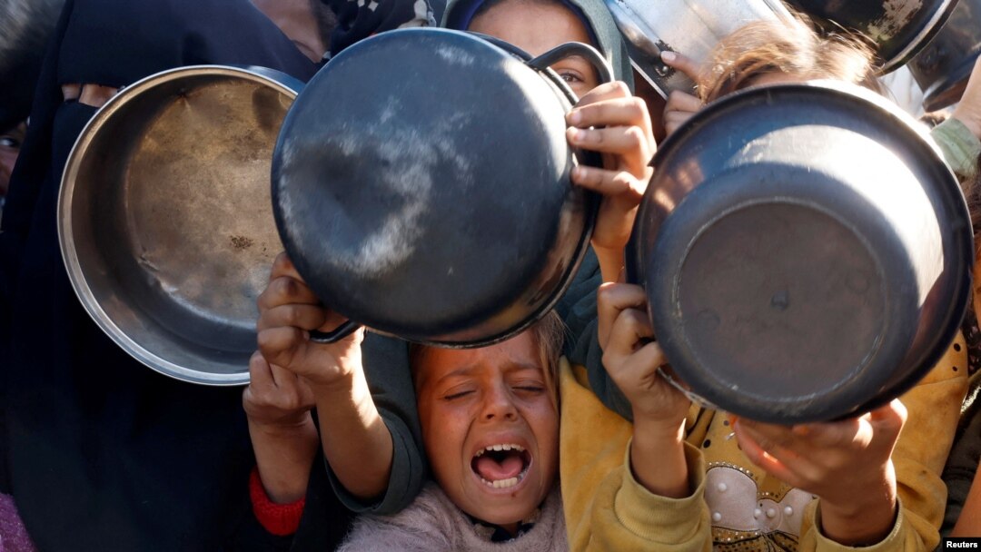 Palestinianos reúnem-se para receber alimentos confeccionados por uma cozinha de caridade, no meio de uma crise de fome, em Khan Younis