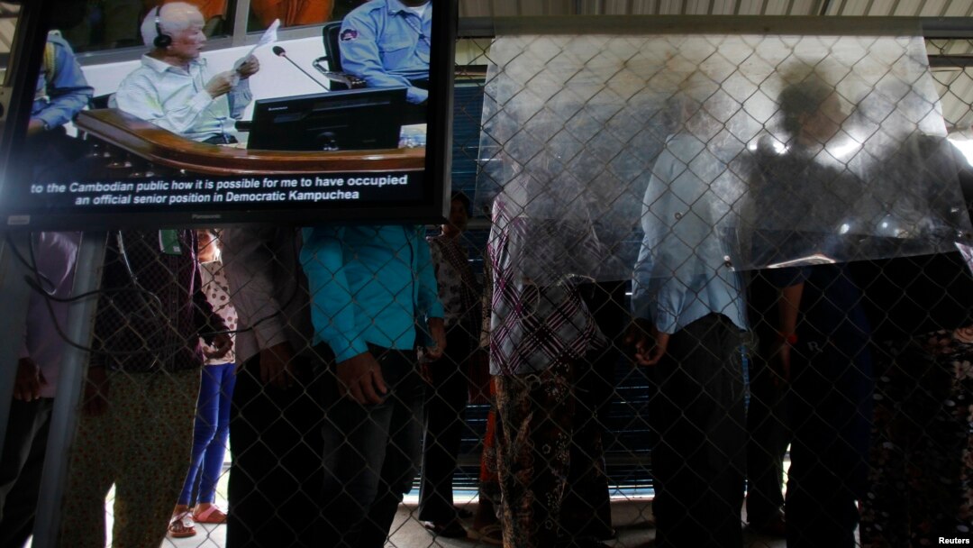 FILE - People line up to enter the Extraordinary Chambers in the Courts of Cambodia as a television screen shows former Khmer Rouge President Khieu Samphan, in Phnom Penh.