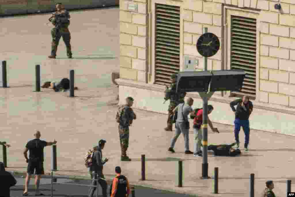 French police point a gun at a man on the ground (C) as a stabbed woman lies (L) while soldiers secure the area following an attack at the Saint-Charles main train station in the French Mediterranean city of Marseille. A suspected Islamist man killed two women at the main train station in Marseille before being shot dead by soldiers on patrol, local officials and police said.