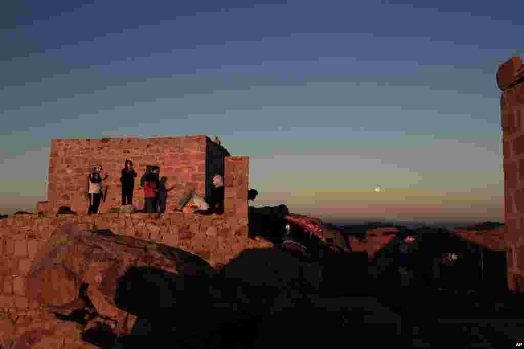 Arab tourists, left and American tourists, right, watch the sun rise and the moon set from the top of Mount Sinai or 'Mount Moses' in Saint Catherine in the Sinai peninsula, Egypt.