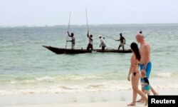Tourists walk along the beach as fishermen paddle their boat near the shores of the Indian Ocean in Mombasa, Kenya, January 18, 2016.