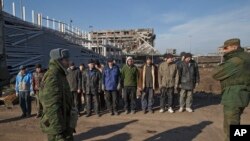 FILE - Ukrainian prisoners of war stand as Russia-backed separatists watch in front of the destoryed airport building outside Donetsk, Ukraine, Feb. 25, 2015.