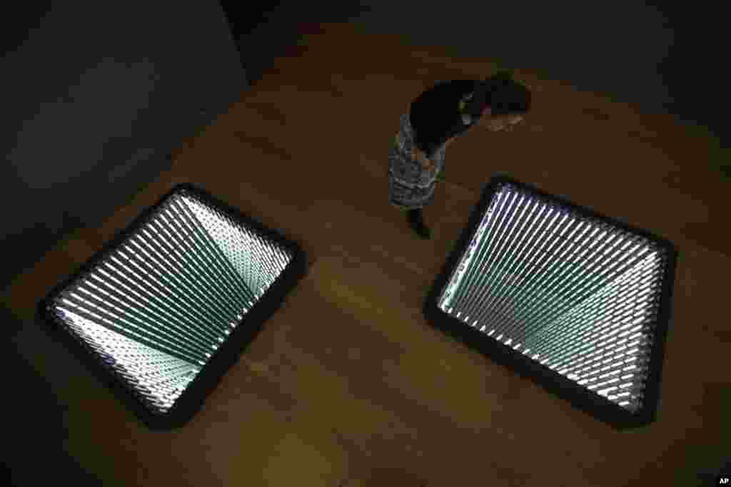 A staff member poses for photographs looking at Chilean-born artist Ivan Navarro's two light box and mirror installation "The Twin Towers" during the media preview for the "Age of Terror: Art since 9/11" exhibition at the Imperial War Museum in London.