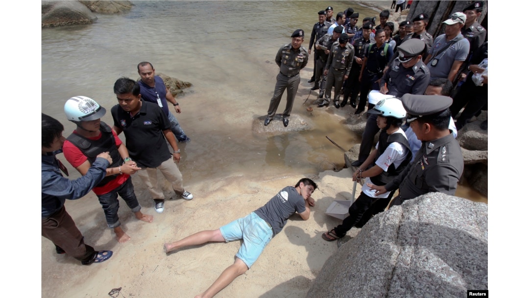 FILE - Two workers from Myanmar (wearing helmets and handcuffs), suspected of killing two British tourists on the island of Koh Tao last month, stand near Thai police officers during a re-enactment of the alleged crime.