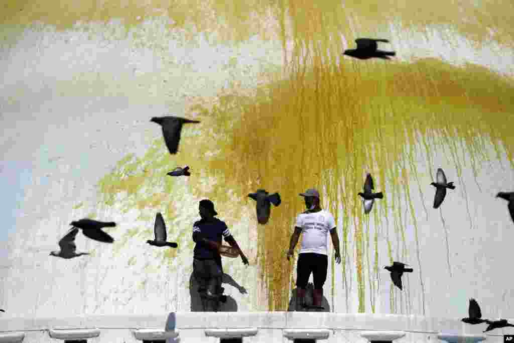 Pigeons fly past Nepalese workers splashing color on the Boudhanath Stupa in Kathmandu, Nepal.