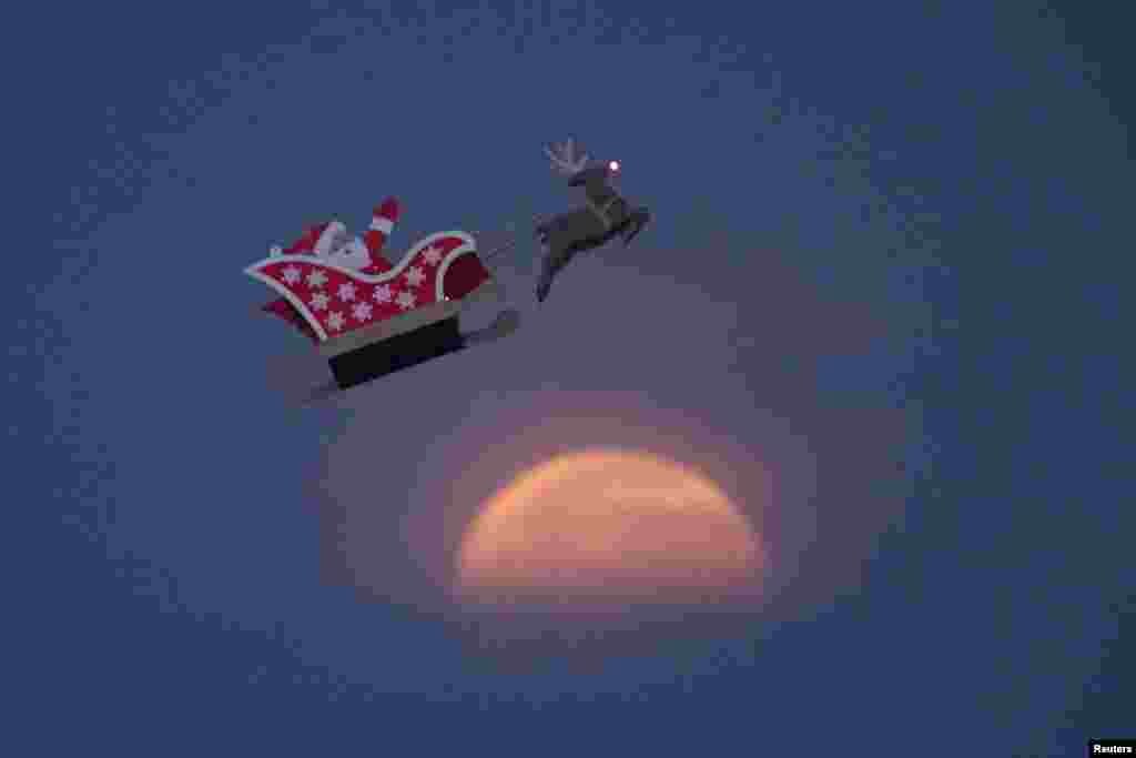 A 10-foot long remote-controlled flying Santa makes a test flight past a setting moon over the ocean in Carlsbad, California.