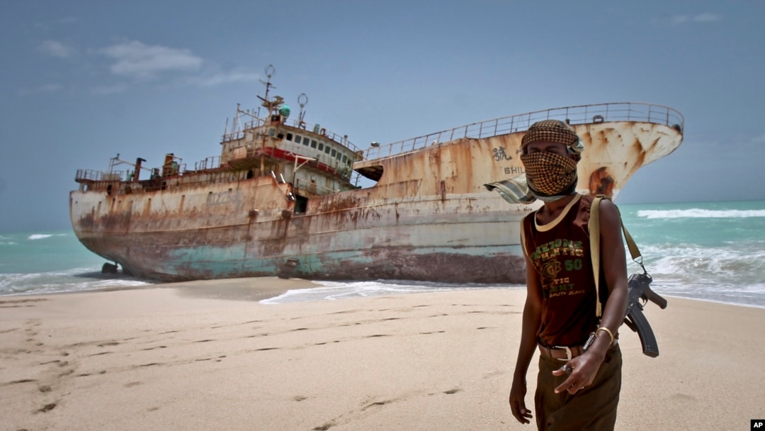 FILE - A masked Somali pirate stands near a Taiwanese fishing vessel that washed up on shore after the pirates were paid a ransom and released the crew, in the once-bustling pirate den of Hobyo, Somalia, Sept. 23, 2012. 
