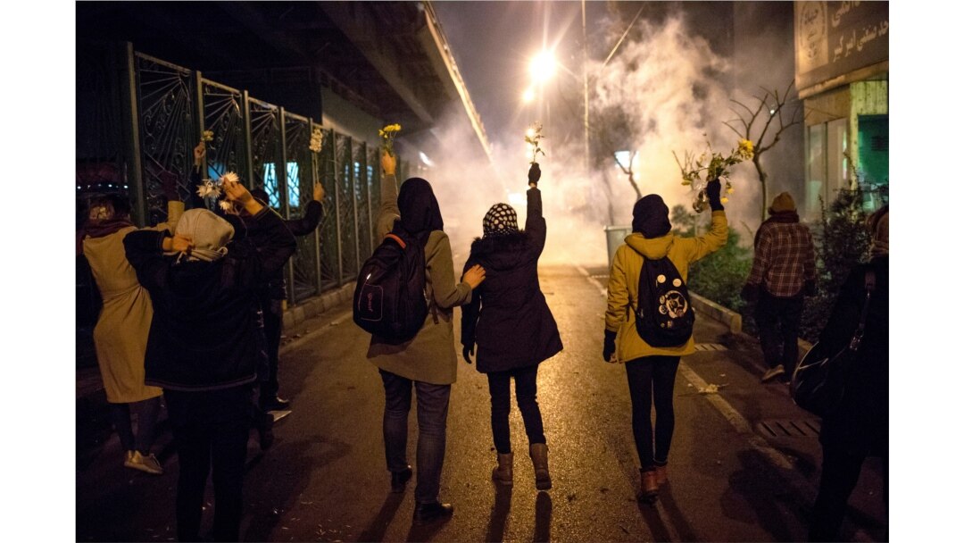 FILE - Protesters hold flowers as tear gas fired by police rises at a demonstration in front of Amir Kabir University in Tehran, Iran, Jan. 11, 2020, to remember victims of a Ukrainian airplane shot down by an Iranian missile.