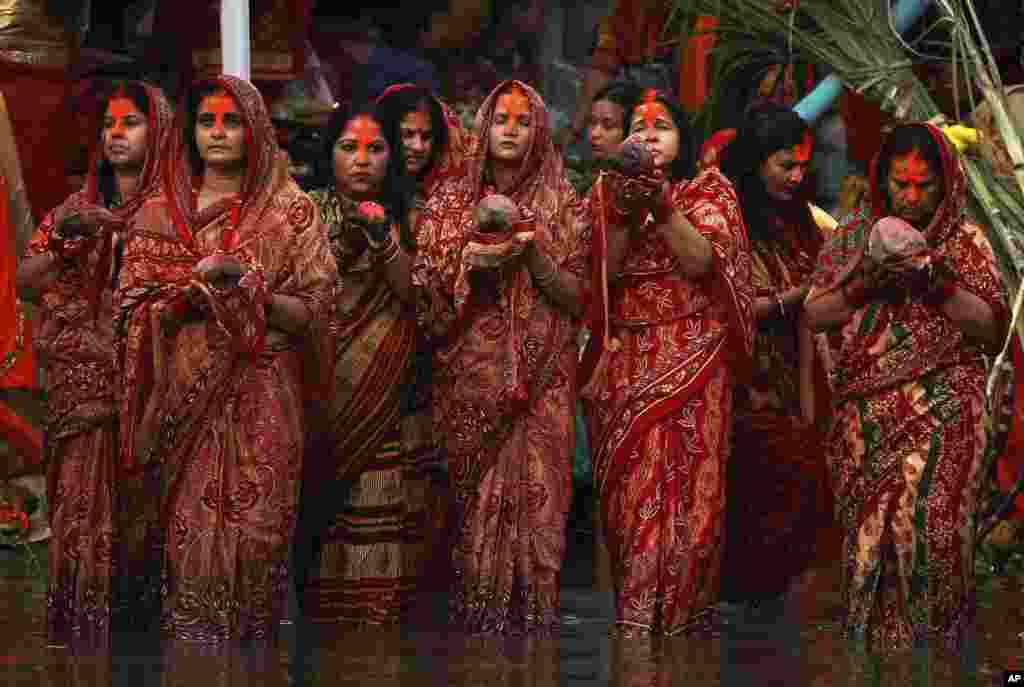 Nepalese women hold coconuts and offer prayers to the setting sun on the banks of the Bagmati River during the Chhath Puja festival in Kathmandu, Nepal.