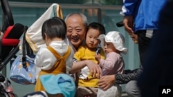 FILE - An elderly man plays with children near a commercial office building in Beijing on May 10, 2021.