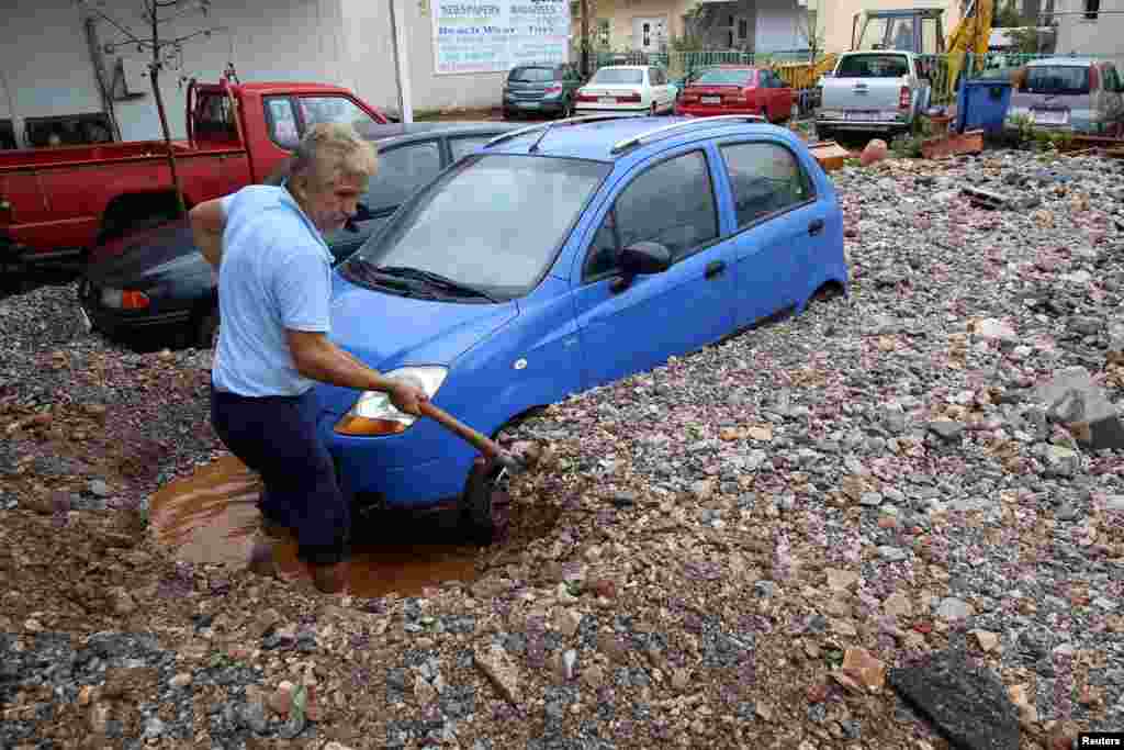 A local shovels mud blocking a car, following heavy rainfall in Malia on the island of Crete, Greece.