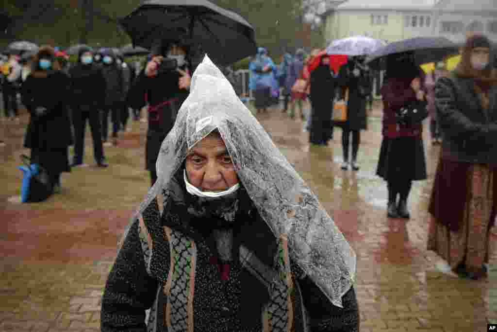 A woman using a plastic sheet as rain protection attends a religious service celebrating St. Andrew in the village of Ion Corvin, eastern Romania. Braving wintry weather and the new coronavirus fears, several hundred Orthodox Christian believers gathered outside a cave where St. Andrew is said to have lived and preached in the 1st century. 